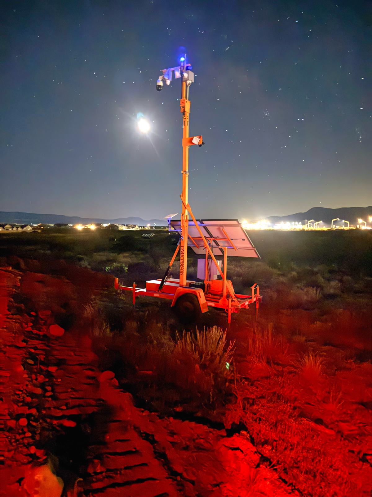 A Guardian Rover 360 surveillance trailer with its mast fully extended on an Arizona jobsite at night, stars overhead and town lights on the horizon.