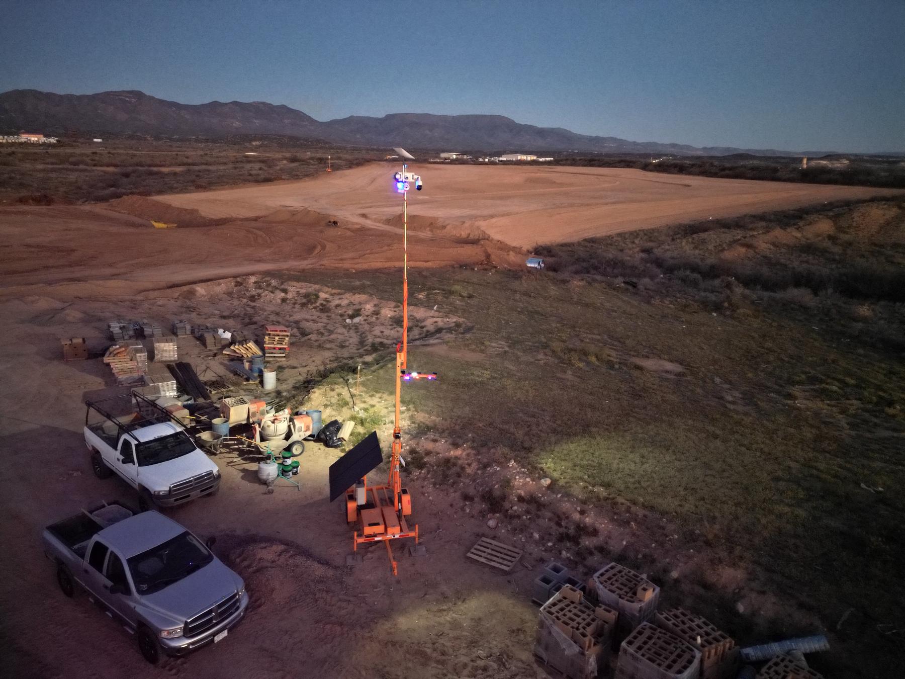 Aerial view of an Arizona development site at dusk with a Guardian Rover 360 trailer overlooking graded pad, material laydown, and parked trucks.